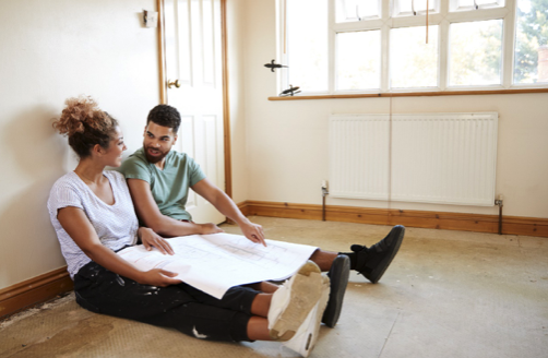 Couple smiling and sitting in their house they are renovating