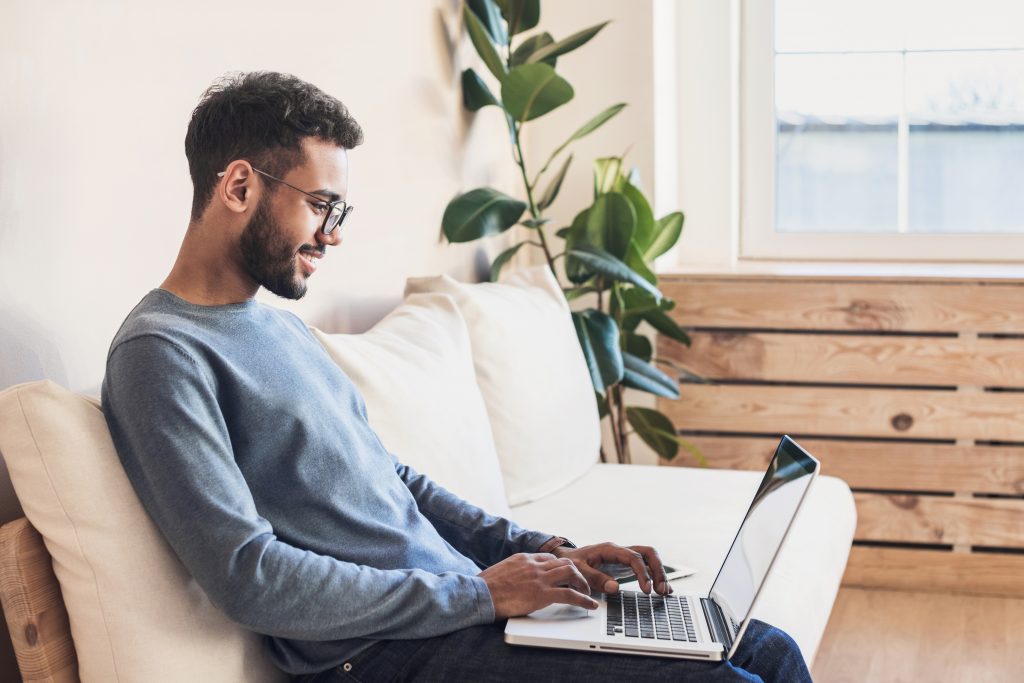 Man sitting on white couch typing on laptop on his lap