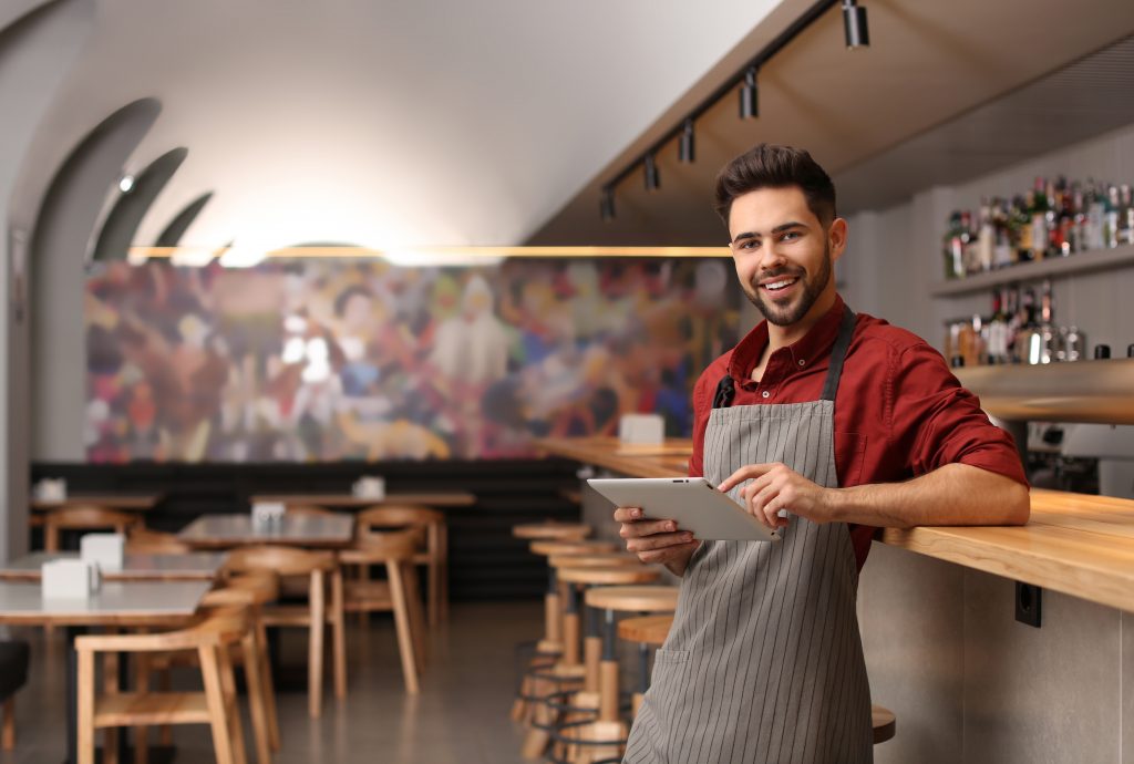 Young male business owner with tablet near counter in his cafe