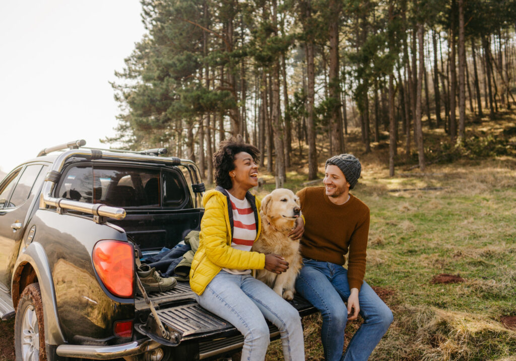 couple with a golden retriever sitting in their pickup truck bed
