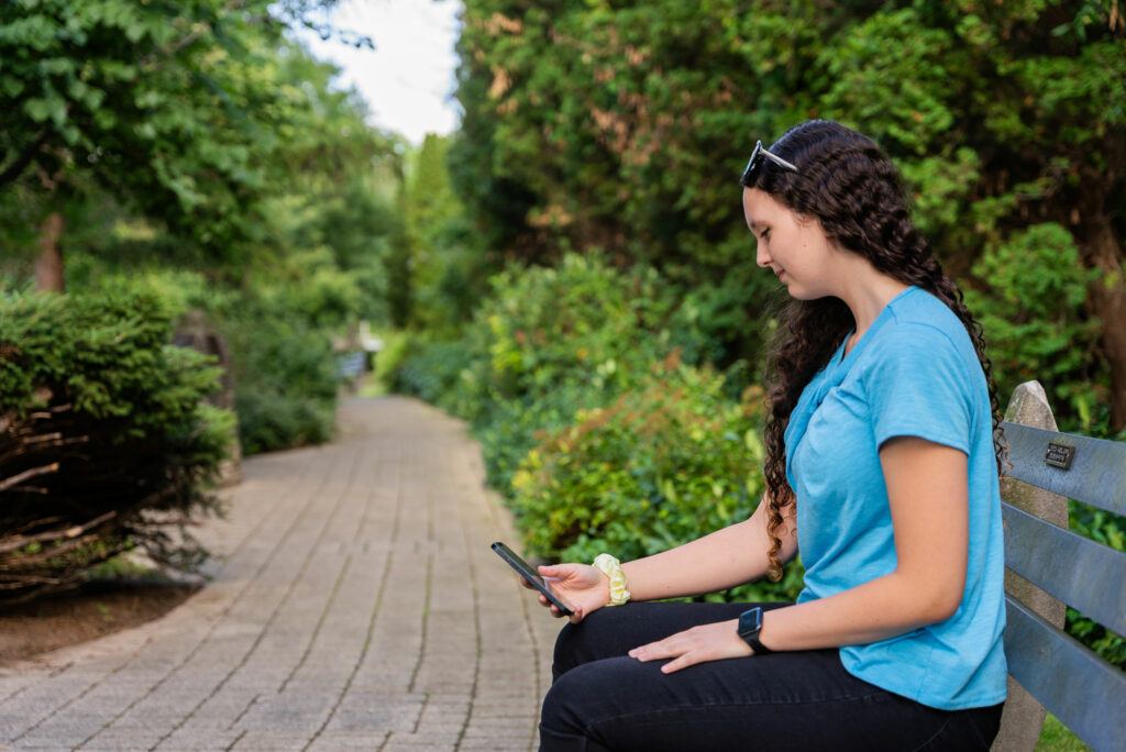 Libro Member Lexxeigh sitting on a bench in the park looking at her phone