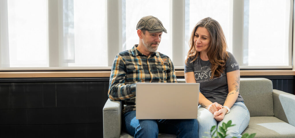 Libro Business Owners, Caps Off Brewing Co., sitting on a couch together looking at a laptop