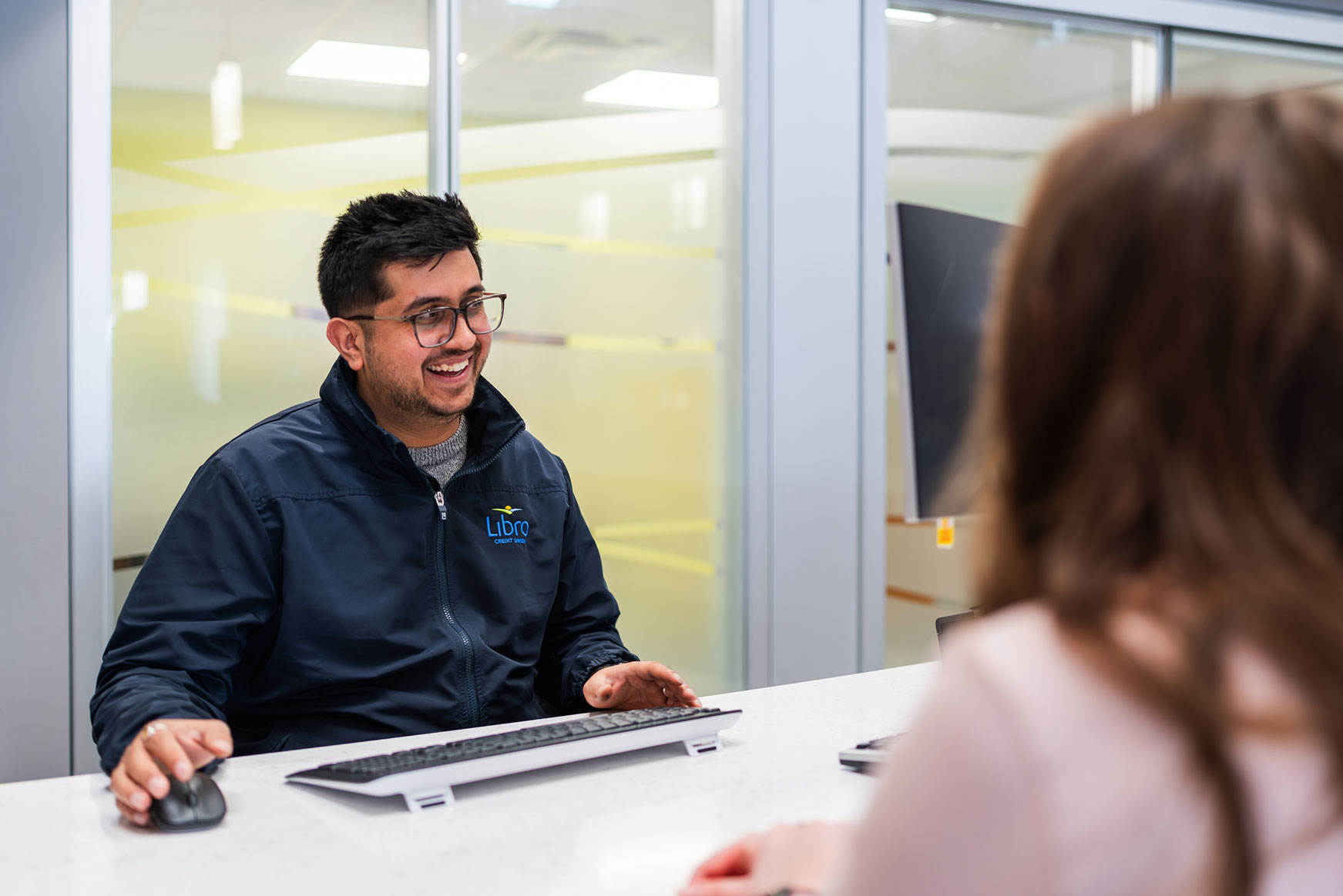 A Libro Staff sitting at a wicket talking to a Libro Member