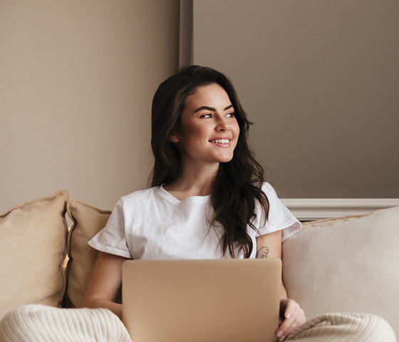 A woman on a laptop looking out the window and smiling