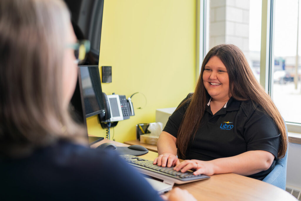 Libro Watford Staff Member sitting behind a desk and smiling at a Libro Member
