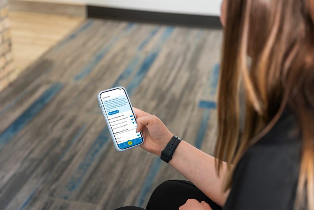 A person holding a smartphone and reading a conversation on a messaging app while sitting on a gray and blue carpeted floor.