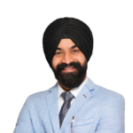 A man wearing a black turban, light blue suit, white shirt, and tie, smiling with arms crossed against a white background.