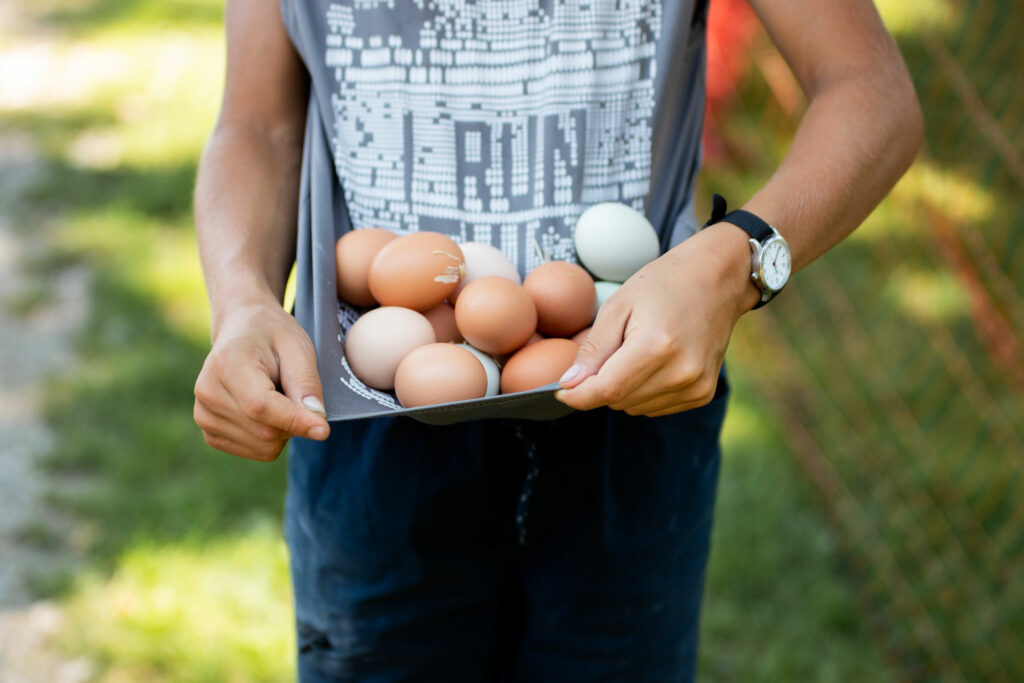 Person holding a tray filled with brown and light green eggs outdoors, wearing a sleeveless shirt and a watch.